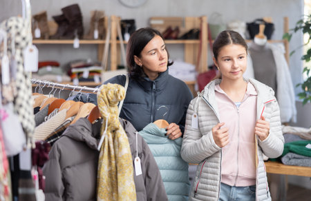 Adolescence girl try on down jacket during shopping with mother in clothes storeの写真素材