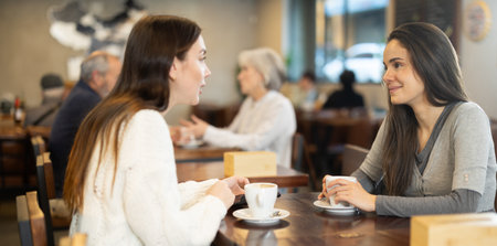 Two young women drinking coffee and talking in cafeの写真素材