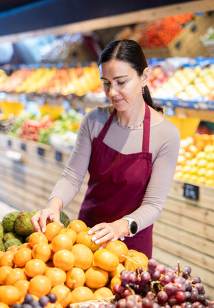 Female supermarket employee checks oranges on shelvesの写真素材