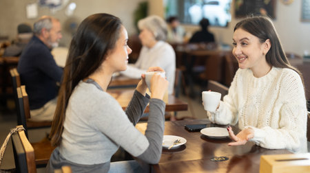 Two young women drinking coffee and talking in cafeの写真素材