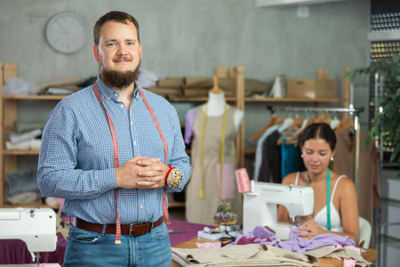 Male dressmaker welcoming clients while young seamstress is sewing behindの写真素材