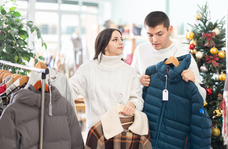 Couple standing in shop and choosing warm winter clothes in Christmas shopの写真素材