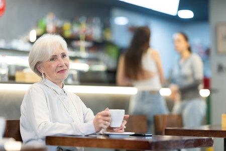 Eldery woman drinks coffee in cafe