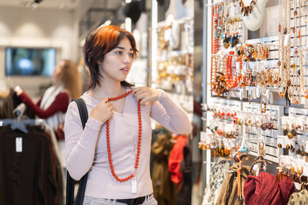 Attentive young girl choosing necklace in clothing storeの写真素材