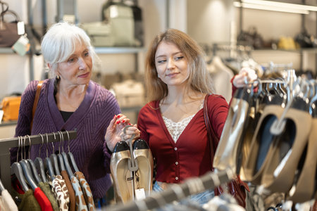 Positive girl and mature woman choosing shoes in clothing storeの写真素材