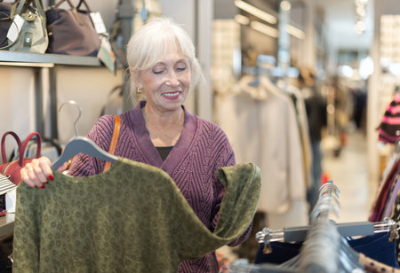 Eldery woman chooses sweatshirt in clothing storeの写真素材