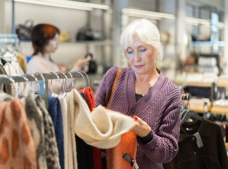 Aged woman choosing a wool scarf in the storeの写真素材