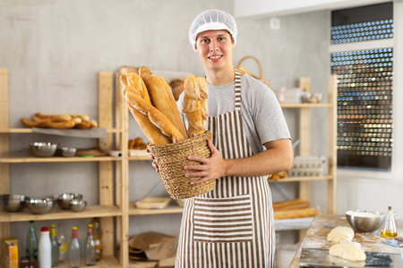 In working room of bakery, there is man with baguettes in wicker basket in hands