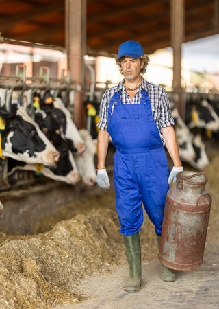 Middle-aged male farmer carrying metal milk tankの写真素材