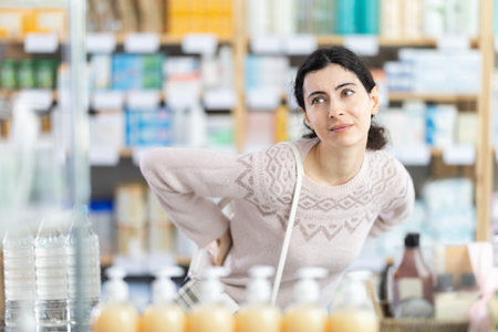 Girl suffers from back pain - looks for medicine in modern pharmacy
