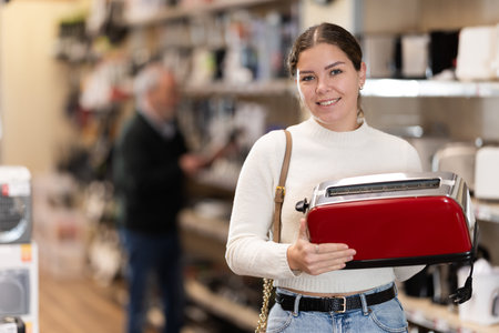 Positive young woman choosing toaster in hypermarket