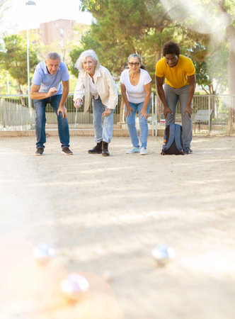 Company of friendly mature people playing petanque in park