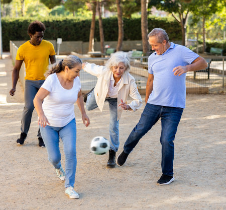 Joyful senior multinational friends playing soccer on a sandy playground on a warm spring eveningの写真素材