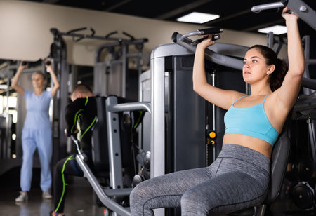 Athletic woman is engaged in simulator - develops biceps and triceps