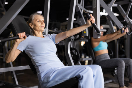 Focused mature female athlete using chest press machine in gymの写真素材