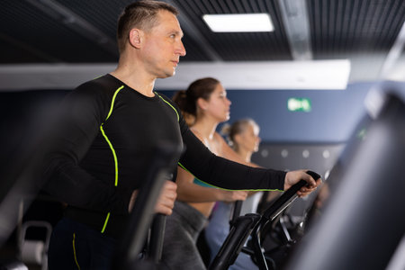 Strong sportsman training at elliptical machine in gym