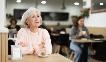 Elderly woman sitting at a table in a coffee shop with a cup of aromatic coffeeの写真素材