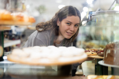 Girl employee puts croissants in window, arranges display of goodsの写真素材