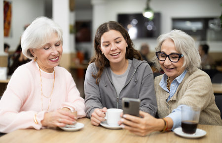 Happy young girl meeting and celebration with family, showing photos on phone over dinner in restaurantの写真素材