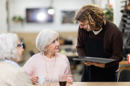 Waiter listens attentively to orders of elderly cafe patronsの写真素材