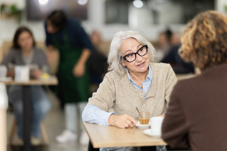 Positive grandmother in cafe sits near adult son, has nice conversation and discusses news of dayの写真素材