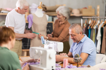 Mature man and woman sew and talking, others senior people work with mannequin at sewing school...