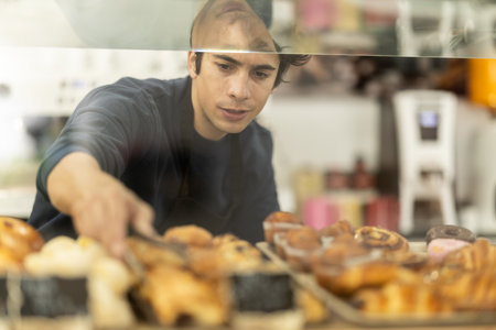 Male seller putting fresh pastries on plate in cafe bakeryの写真素材