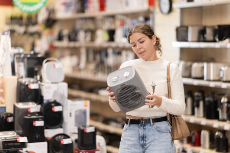 Young woman chooses portable heater in appliance storeの写真素材