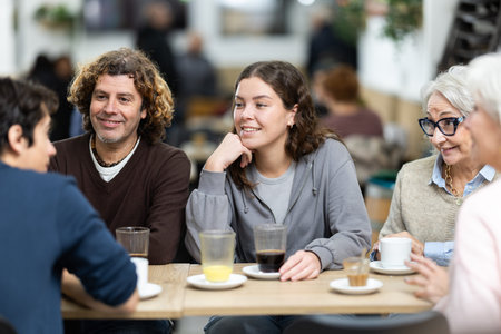 Large family is having breakfast in a cozy cafe, discussing news.