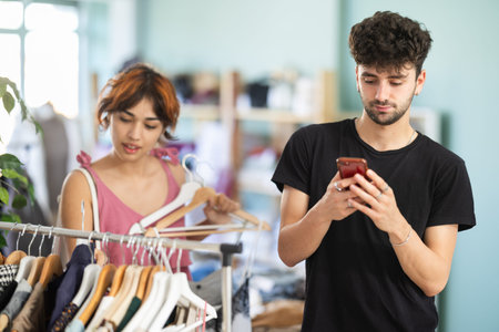 Guy immersed in phone while girlfriend choosing dresses in store