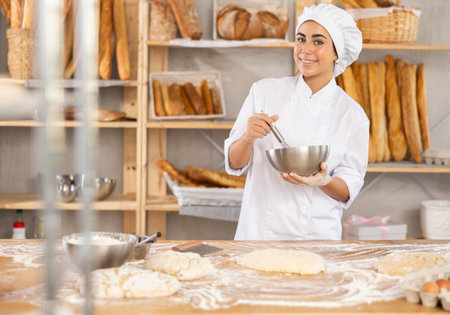 Young female baker whisking dough in bowl