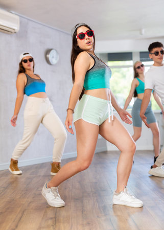 Group of young girls in dark glasses and ball cap dance shuffle in fitness club
