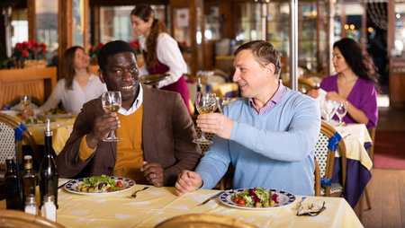 Two cheerful men having dinner in cozy restaurant