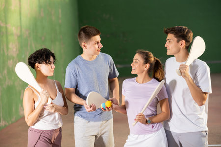Group of young men and women having conversation about paleta fronton game on court