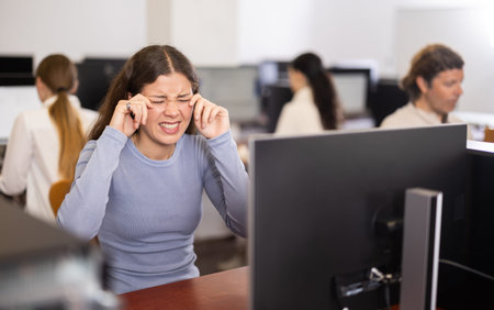 After working on computer, girl rubs tired eyes