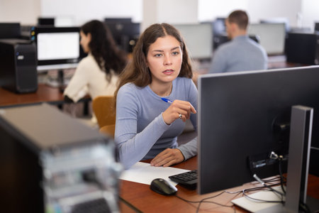 Female student looks at monitor screen, write down note in notebook