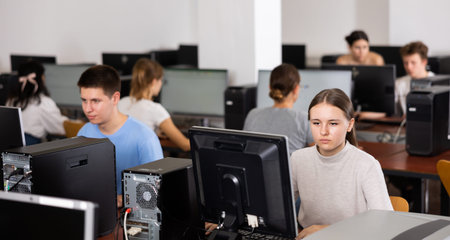 Focused teenager students sitting at desk in computer room with pc, preparing for exam. Focus on...