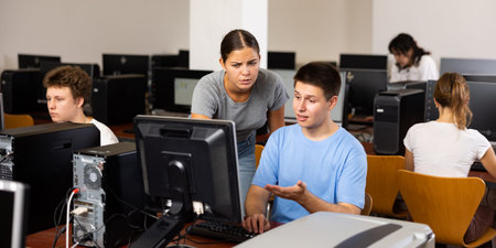 Focused female teenager giving a clue to the male co-learner while he is using pc in the computer...