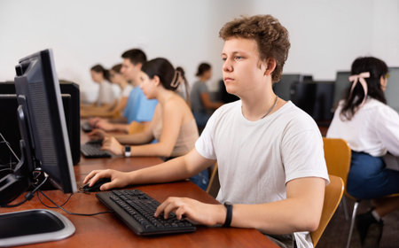 Smart male teen learning computer science while he is using a PC in the computer classroom