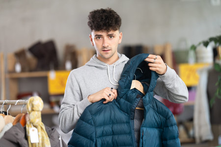Young guy choosing down jacket in clothing store