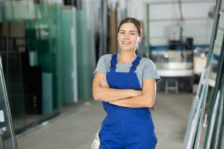 Portrait of positive girl in a blue overalls in window glass production workshopの写真素材