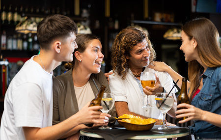 Spending time in bar. Four positive friends drinking beerの写真素材
