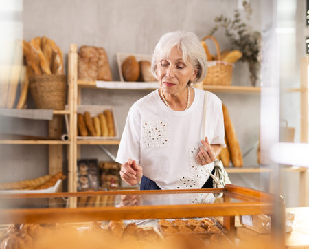 Mature female customer choosing croissants in bakeryの写真素材