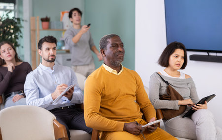 Students of different ages listen attentively to teacher and take notes in notebooks during a lecture at the learning center.の写真素材