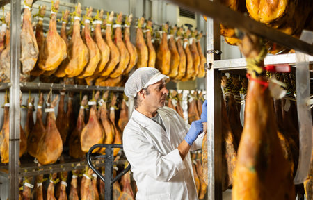 Male worker at ham factory checks the quality of ham in workshopの写真素材