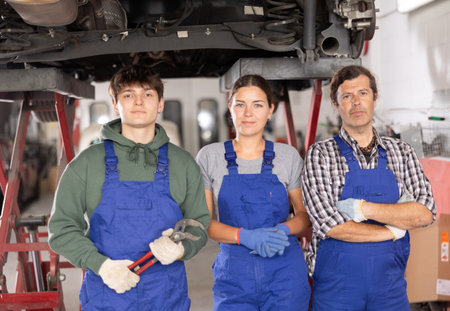 Guy, woman and man mechanics posing in car repair shopの写真素材