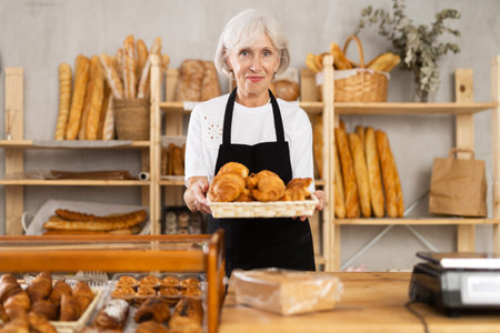 Senior woman seller of bakery store is standing in trading floor, waiting for visitorsの写真素材