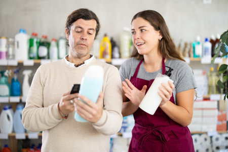 Saleswoman offering shower gel to man scanning barcode of bottles in storeの写真素材