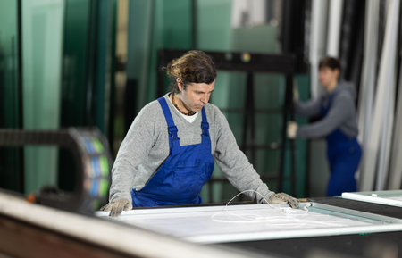 Adult man puts sheet of glass for processingの写真素材