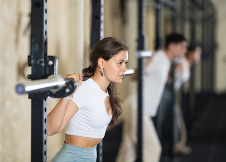 Girl in activewear exercising with barbell during group workout in gym center